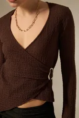 Top de manga larga color negro, con diseño cruzado, escote en V profundo y detalle de argolla lateral. Presenta una textura rugosa y corte asimétrico en el ruedo.
