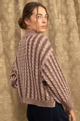 Sweater de punto con diseño de trenzas verticales, cuello alto y corte holgado. Presenta mangas largas con puños acanalados y un largo a la cadera.