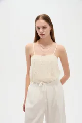 Musculosa de poliéster color marfil, con tirantes finos regulables, cuello cuadrado y diseño holgado, decorada con bordados de estrellas.