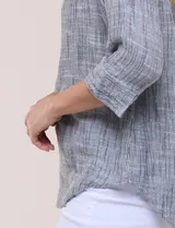 Blusa de silueta relajada con textura tramada, color azul con rayas verticales en tonos rosados, celestes y amarillos. Cuenta con cuello mao abierto en V y mangas tres cuartos amplias con pequeña abertura lateral en el puño.