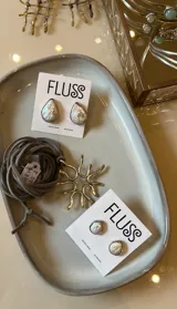 Collar artesanal con dije de diseño orgánico en metal y tiento de gamuza ajustable. El dije presenta una forma circular con terminaciones curvas, evocando un diseño natural.