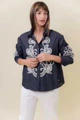Camisa de denim liviano color azul oscuro con bordado artesanal en tono crudo en el frente y en las mangas. Presenta cuello clásico y cierre frontal con botones, con un calce relajado.