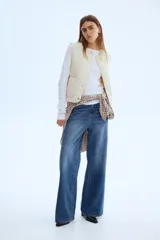 Chaleco guateado color beige, con cuello redondo, cierre frontal con botones a presión y dos bolsillos de parche en la parte delantera. Sin forrar.