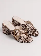Sandalias de taco ancho marca Aura, confeccionadas en cuero vacuno con estampa tipo animal print de vaca en tonos marrones y blancos. Poseen capellada cruzada con hebilla metálica dorada y taco forrado al tono.