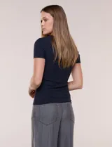 Remera básica de modal elastizado color blanco, con textura acanalada fina, escote redondo y mangas cortas. Presenta un pequeño logo metálico aplicado cerca del ruedo frontal.
