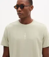 Remera de algodón color verde claro, de corte regular, cuello redondo y manga corta. Presenta un estampado náutico de un ancla y letras en el pecho.