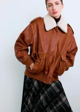 Chaqueta estilo aviador de cuero sintético marrón, con cuello de corderito sintético blanco, bolsillos frontales con solapa, cierre de cremallera y puños y cintura de canalé elástico.