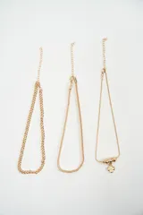 Set de tres brazaletes dorados de diferentes estilos: uno de cadena gruesa, uno de cadena fina tipo serpiente y uno de cadena fina con dije de trébol y cuentas esféricas.