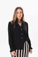 Camisa de manga larga color negro, con cuello camisero, cierre frontal con botones y detalle de volados en la cartera y los puños.