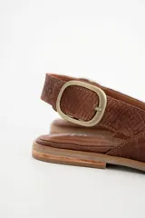 Sandalia chata color marrón con textura tejida, punta fina y tira trasera con hebilla dorada.