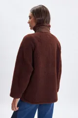 Campera de sherpa color marrón con cuello alto, cierre frontal con botones a presión y detalles en tela técnica a tono. Presenta un bolsillo vertical con cierre en el pecho y dos bolsillos laterales con cierre.