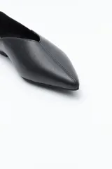 Zapato bajo de mujer, color negro, con punta fina y escote pronunciado en forma de V en el empeine. Presenta un acabado liso y una suela baja y plana.