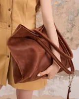 Bolso tote de cuero marrón con costuras a la vista y charm de flecos colgando de una cadena.