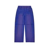 Pantalón baggy color azul con efecto lavado, presenta un aplique bordado con la palabra 'Valley' decorado con cristales de colores. Incluye detalles de tachas multicolores a lo largo de las costuras laterales y en el ruedo, cintura elástica con cordón de ajuste y costuras horizontales a la altura de las rodillas.