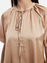 Blusa de satén color tostado con cuello redondo, cierre frontal con cordones ajustables y mangas cortas tipo raglán con diseño holgado.