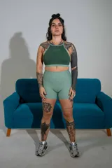 Top deportivo verde oscuro de doble tela, con cuello halter, espalda cruzada y banda elástica inferior en tono más claro. Cuenta con el logo de la marca estampado en el centro del pecho.