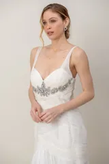 Vestido largo de gasa color marfil, con escote en V, drapeado en el torso y detalle de bordado en pedrería bajo el busto, falda amplia tipo godet y tiritas anchas.