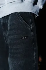 Pantalón de jean estilo baggy color negro con efecto lavado, corte holgado y diseño de cinco bolsillos. Presenta un pequeño dije decorativo en la cintura y detalle de logo metálico en el frente.
