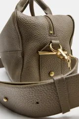 Bolso alargado tipo bowling color verde oliva, confeccionado en cuero con doble asa de mano y asa bandolera extraíble. Incluye bolsillo interior con cremallera y cierre principal con cremallera.