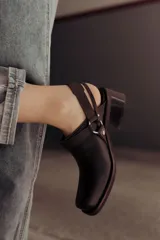 Zuecos de cuero color marrón oscuro, con diseño cerrado en la parte delantera, tira ajustable con hebilla metálica en el talón y taco cuadrado bajo.