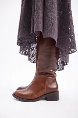 Bota de caña alta confeccionada en cuero vacuno, con taco cuadrado bajo y punta redondeada.