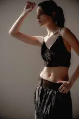 Top corto de encaje negro con breteles finos, diseño ajustado y detalles de terciopelo. Incluye apliques de plumas desmontables.