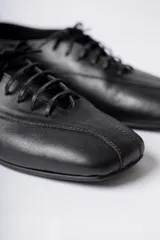 Zapato acordonado de cuero color negro, de diseño minimalista con punta cuadrada y silueta moderna.