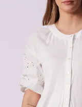 Blusa de color blanco con torso de modal y mangas cortas con detalle de bordado calado. Presenta cuello redondo con apertura central abotonada.