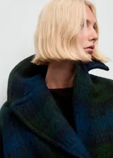 Abrigo de corte oversize con diseño de cuadros en tonos azul y verde. Presenta cuello con solapas, cierre frontal con botones, bolsillos laterales y manga larga.