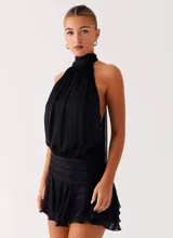 Vestido corto negro con cuello halter, espalda descubierta y falda de volados, confeccionado en tela liviana con cintura elastizada.