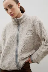 Campera de sherpa color beige con cuello alto, cierre frontal completo y bordado a contra tono en el pecho.