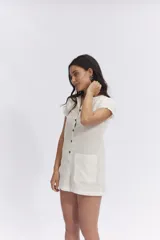 Mono corto color crema, de lino, con cuello camisero, mangas cortas y cierre frontal con botones.