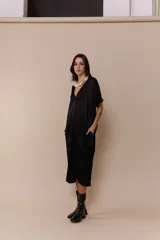 Vestido negro de corte midi, con escote en V y mangas cortas amplias. Presenta un cuello blanco con volados.
