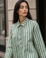 Sobrecamisa de diseño holgado con estampado de rayas verticales en tonos verde, blanco y marrón. Cuenta con cuello camisero, cierre frontal con botones metálicos a presión y bolsillos aplicados en el pecho.