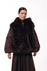 Campera de invierno con frente de piel sintética y capucha integrada, combinada con mangas acolchadas de estilo puffer en color marrón oscuro.