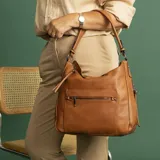 Cartera tipo hobo de cuero sintético color rojo ladrillo, con correa de hombro ajustable. Tiene cierre superior con solapa y broche magnético, bolsillo frontal con cierre, bolsillos laterales con cierre y múltiples bolsillos internos.