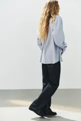 Camisa oversize de manga larga con cuello solapa, cierre frontal de botones y bolsillo de parche en el pecho, con diseño de rayas verticales celestes y blancas.