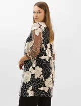 Conjunto de tres piezas compuesto por una musculosa negra con escote en V, un pantalón palazzo de tejido de punto liso con cintura elástica y una túnica larga de tul negro con mangas 3/4. La túnica presenta un bordado floral detallado con aplicaciones de lentejuelas.