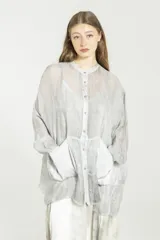 Camisa de viscosa y seda gris, de corte boxy y diseño semitransparente. Posee cuello mao, cierre frontal con botones, mangas largas con puños, bolsillos grandes en el frente y detalles de satén.