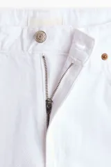 Pantalón jeans blanco de corte baggy y tiro alto, confeccionado en denim rígido de algodón. Presenta diseño de cinco bolsillos, bragueta con cierre y botón, y perneras amplias de corte recto.