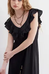 Vestido largo negro de escote redondo con volados decorativos que recorren el frente y la espalda. Presenta un cordón de ajuste en la cintura con terminaciones metálicas y espalda baja.