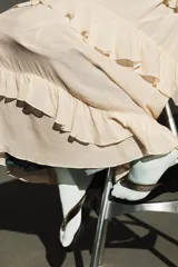 Vestido midi de escote en pico con lazada frontal y diseño sin mangas. Presenta múltiples niveles de volantes a lo largo de la falda y cierre lateral con cremallera oculta.