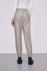 Pantalón tipo babucha de eco cuero color cemento, con cintura elástica y cordón de ajuste, bolsillos laterales y puños elásticos en los tobillos.