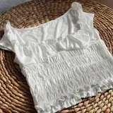 Top blanco con escote asimétrico, bretel fino y volados en el escote y en el ruedo. El torso es elastizado.