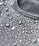 Pantalón de jean modelo wide leg color gris, con cintura tradicional, bolsillos funcionales y detalle de aplicaciones de brillos en la parte superior.