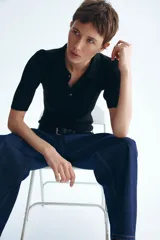 Top de punto pointelle acanalado en color negro, con cuello camisero, manga corta y tapeta con botones frontales.