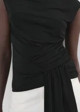Top negro sin mangas con cuello perkins, detalle fruncido en la cintura y panel drapeado colgante en el frente.