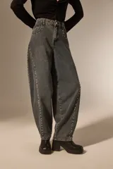 Pantalon de jean estilo barrel con lavado oscuro, tiro medio y detalle de tachas metálicas a lo largo de las costuras laterales.