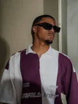 Chomba de piqué con diseño color block vertical en negro y verde oscuro, cuello polo y cierre frontal parcial. Presenta inscripciones en el frente.