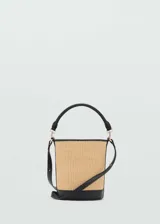 Bolso tipo bucket de tamaño pequeño con cuerpo de rafia y detalles en cuero sintético negro. Cuenta con asa de mano fija, correa bandolera ajustable y extraíble, y cierre superior.